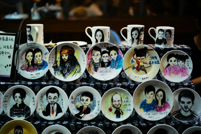 Plates and mugs with painted portraits displayed for sale.